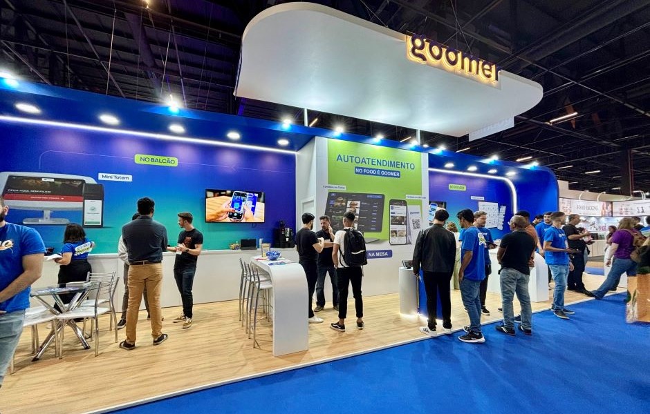 Visitantes na feira de tecnologia interagindo com sistemas de autoatendimento no espaço de autoatendimento de um evento de tecnologia, destacando inovação e atendimento ao cliente.