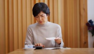 Mulher lendo uma carta sentado em uma mesa de madeira, ambiente acolhedor com paredes de madeira e uma planta ao fundo, expressão pensativa.