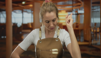 Mulher com avental levantando o dedo em sinal de ideia ou celebração, dentro de um ambiente moderno e acolhedor, possivelmente uma cafeteria ou escritório.