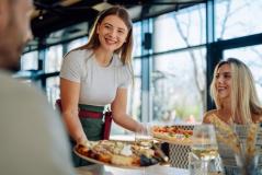 Garçonete entregando pizzas a clientes felizes em um restaurante moderno, proporcionando uma experiência gastronômica agradável e cordial.