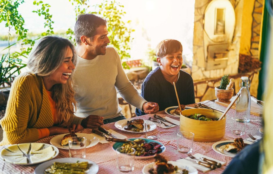 Uma família sorridente se reunindo para o jantar, com pratos de comida em uma mesa decorada, em um ambiente aconchegante.