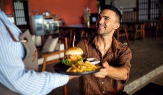 Homem sorridente recebendo um prato de hambúrguer e batatas fritas em um restaurante aconchegante, celebração de momento feliz e refeição deliciosa.