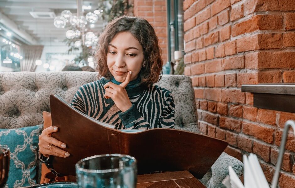 Mulher pensativa analisando o menu em um restaurante aconchegante, refletindo sobre as opções de pratos disponíveis.
