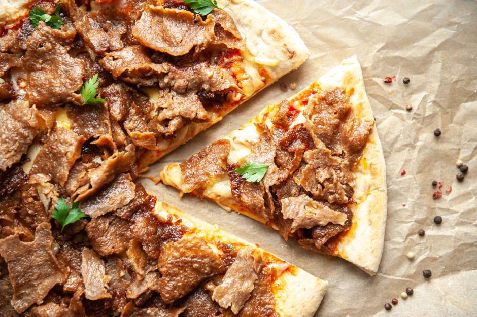 Pizza de kebab sobre um papel pardo com uma fatia destacada