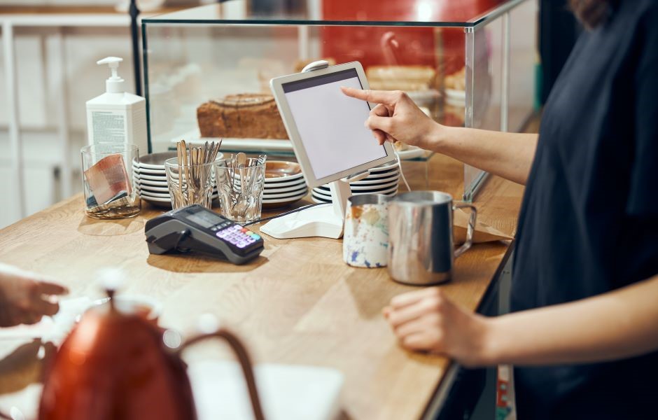 Cliente fazendo pedido em um restaurante pelo dispositivo de controle digital, ao lado de pratos, copos, e utensílios na mesa.