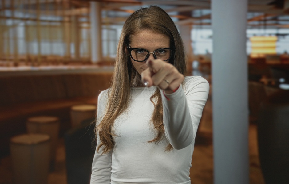 Mulher com óculos apontando para a câmera, destacando-se em um ambiente moderno e acolhedor, ideal para fotos profissionais e retratos.