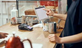 Cliente fazendo pedido em um restaurante pelo dispositivo de controle digital, ao lado de pratos, copos, e utensílios na mesa.