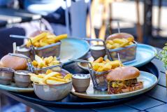 Imagem de uma refeição com batatas fritas e hambúrguer, incluindo molhos e acompanhamentos, servida em um ambiente ao ar livre.