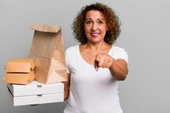 Mulher sorridente segurando embalagens de comida e apontando para a câmera, transmitindo uma sensação de serviço de entrega. Ideal para destacar opções de delivery.