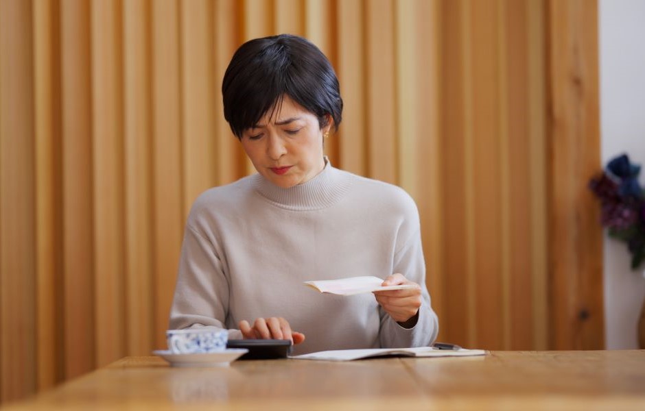 Mulher lendo uma carta sentado em uma mesa de madeira, ambiente acolhedor com paredes de madeira e uma planta ao fundo, expressão pensativa.