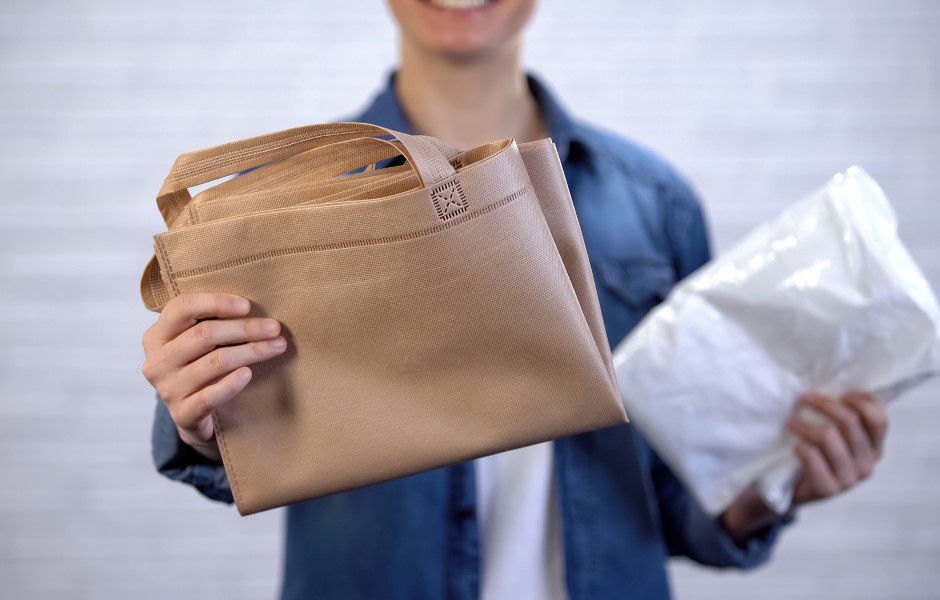 A imagem mostra uma pessoa segurando uma bolsa de compras marrom e um pacote branco. Ideal para destacar a praticidade de usar sacolas reutilizáveis e sustentáveis.