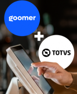 Imagem de um barista sorridente atendendo clientes, com os logotipos do Goomer e TOTVS ao fundo, destacando a parceria entre as marcas