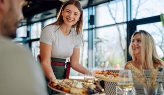 Garçonete entregando pizzas a clientes felizes em um restaurante moderno, proporcionando uma experiência gastronômica agradável e cordial.