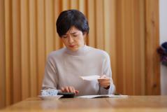 Mulher lendo uma carta sentado em uma mesa de madeira, ambiente acolhedor com paredes de madeira e uma planta ao fundo, expressão pensativa.