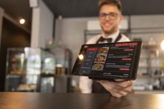 Garçom segurando um tablet com o cardápio digital em um restaurante moderno, mostrando opções de pratos e preços.