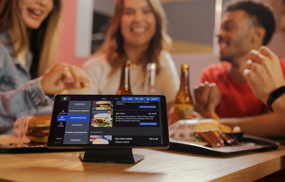 Grupo de amigos se divertindo em um restaurante, com um tablet exibindo o menu e opções de comida, ideal para escolher pratos saborosos juntos.