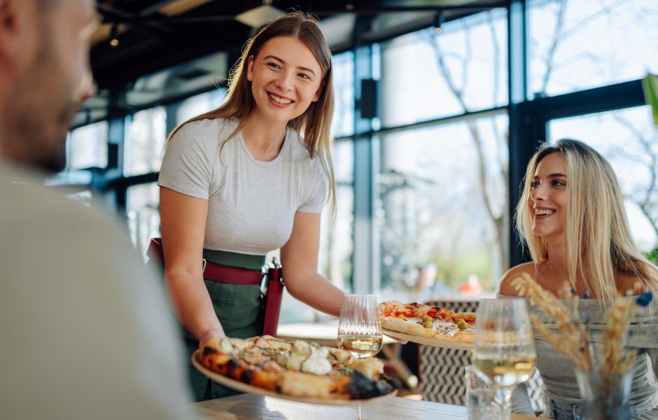 Garçonete entregando pizzas a clientes felizes em um restaurante moderno, proporcionando uma experiência gastronômica agradável e cordial.