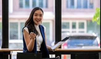 Mulher sorridente em um ambiente de trabalho moderno, sentada em uma mesa com um bloco de notas e um tablet, expressando entusiasmo e confiança.