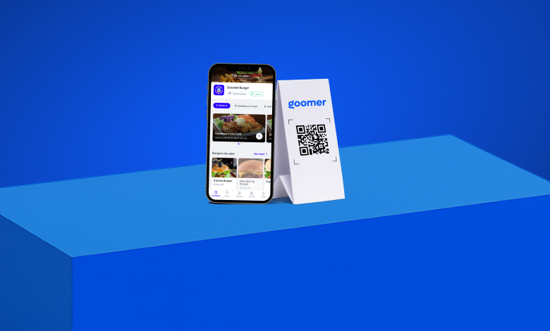Imagem de um smartphone exibindo um aplicativo de delivery de hambúrgueres chamado Goomer, ao lado de um QR code impresso e um fundo azul.