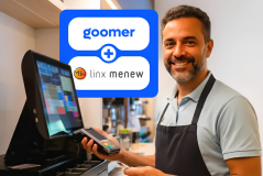Integração entre Goomer e Linx Menew: Homem sorridente em um balcão de restaurante segurando uma maquininha de cartão ao lado de um monitor de PDV.