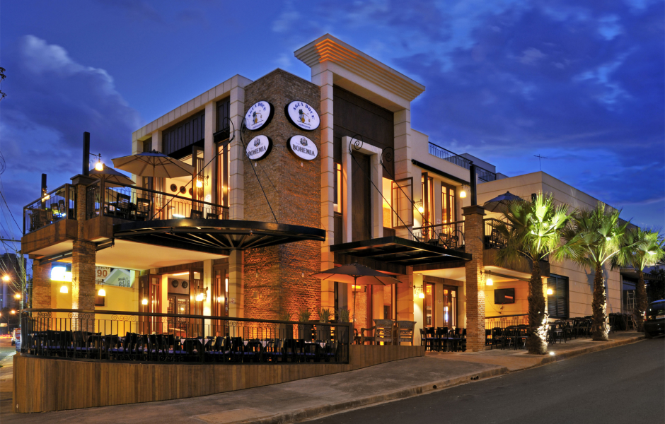Fachada do restaurante Água Doce Sabores do Brasil à noite, com iluminação externa, mesas ao ar livre, guarda-sóis, palmeiras e placas de marcas de cerveja na fachada.