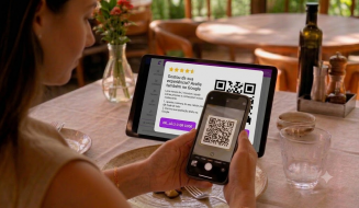 Uma cliente sentada à mesa de um restaurante usa o celular para escanear um QR Code exibido em um tablet. A tela do tablet mostra uma mensagem incentivando a avaliação da experiência do estabelecimento no Google.
