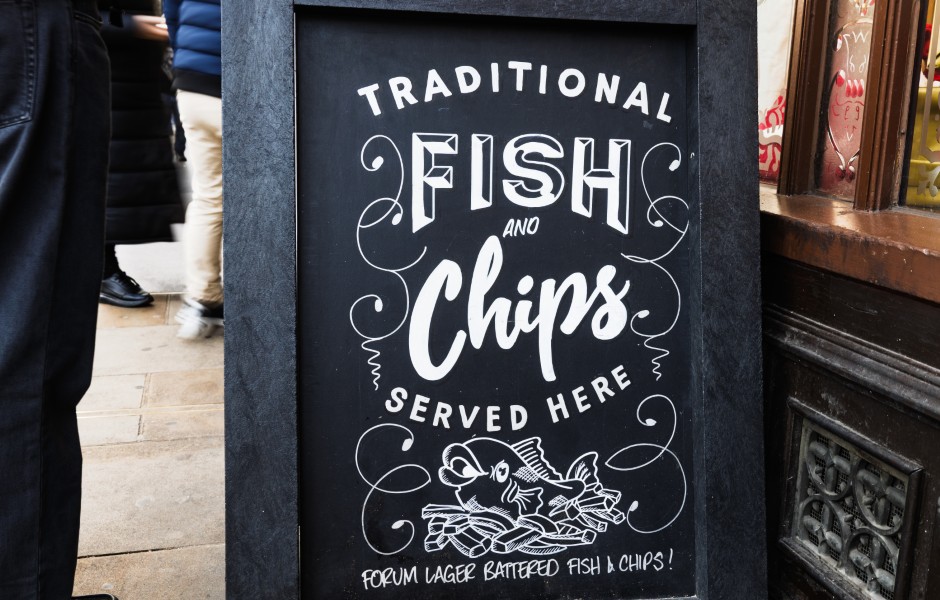 Um quadro de giz que anuncia "Traditional Fish and Chips Served Here" em um restaurante, destacando o prato típico britânico.