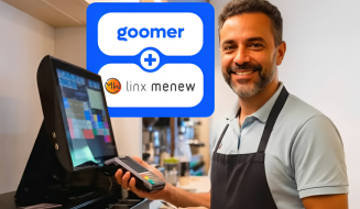 Integração entre Goomer e Linx Menew: Homem sorridente em um balcão de restaurante segurando uma maquininha de cartão ao lado de um monitor de PDV.