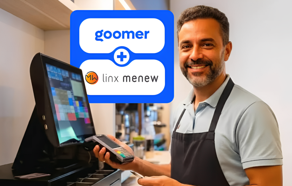 Integração entre Goomer e Linx Menew: Homem sorridente em um balcão de restaurante segurando uma maquininha de cartão ao lado de um monitor de PDV.