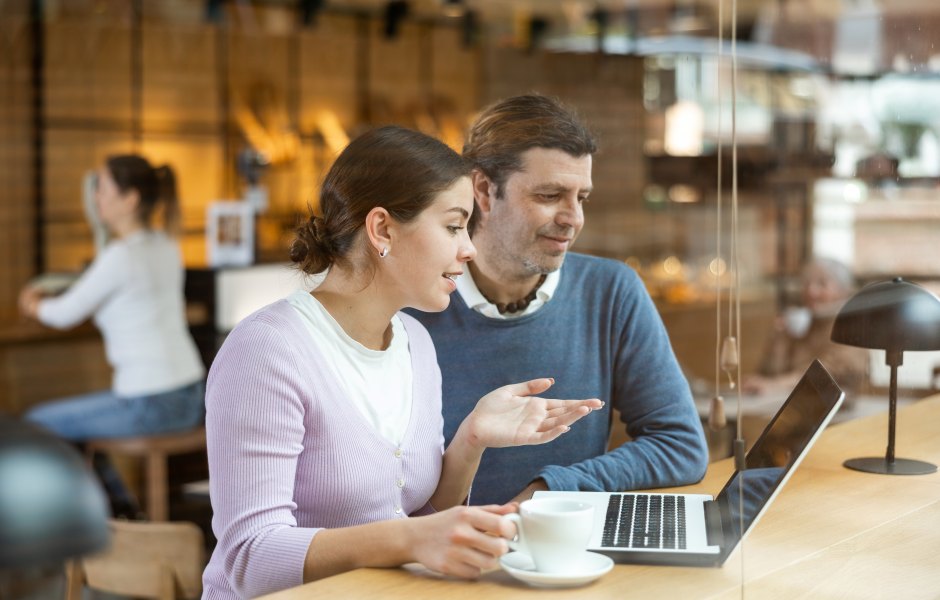 Casal em um café discutindo sobre um projeto no laptop enquanto saboreiam café. Ambiente aconchegante e moderno.