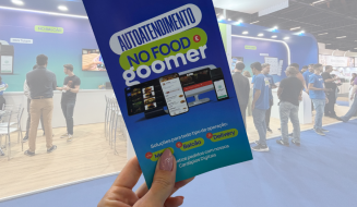 Banner de autoatendimento do NO FOOD e GOOMER em evento de tecnologia, com várias pessoas interagindo com os stands no fundo.