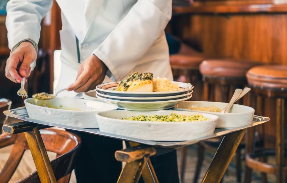 Um garçom em um restaurante serve pratos variados, incluindo arroz e legumes, em uma bandeja.