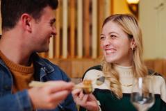 Casal sorridente desfrutando de um momento romântico em restaurante, com destaque para a mulher com cabelo loiro e o homem com cabelo castanho, em um ambiente acolhedor.