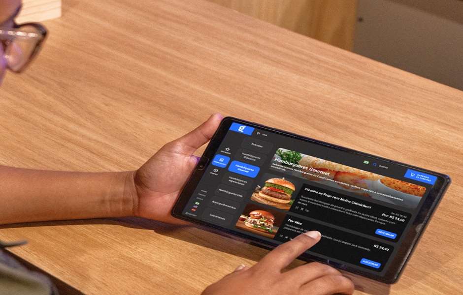 Pessoa usando um tablet para fazer pedidos de hambúrgueres gourmet em um aplicativo de delivery.