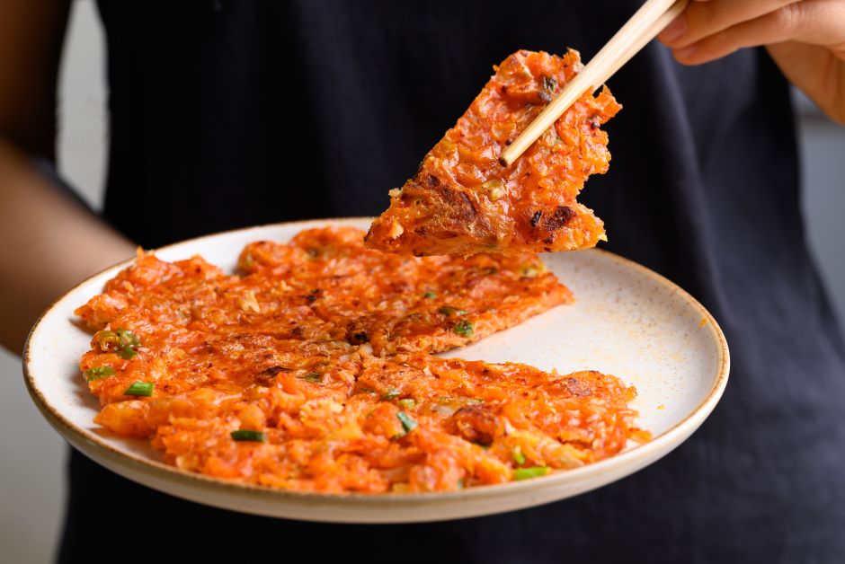 Pizza com Kimchi em um prato e uma fatia sendo segurada em hashi