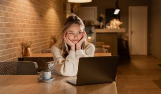 Jovem mulher feliz usando laptop em café aconchegante, focada na tela do computador portátil em um ambiente confortável com iluminação quente.
