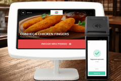 Tela de um sistema de pedidos de comida digital exibindo opções para solicitar pratos, incluindo nuggets de frango, com pagamento aprovado na tela portátil ao lado.