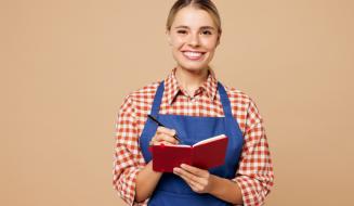 Mulher sorridente usando avental azul segurando um caderno vermelho e uma caneta, em um fundo neutro, representando o dia a dia de um trabalhador. Ideal para conteúdos sobre trabalho e organização.