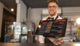 Garçom segurando um tablet com o cardápio digital em um restaurante moderno, mostrando opções de pratos e preços.