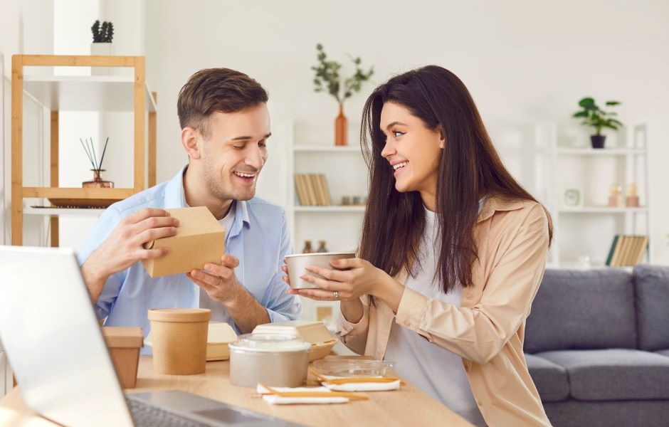 Homem feliz recebendo presente de uma mulher, momento de confraternização e amizade em ambiente de sala de estar moderna com decoração minimalista.