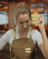 Mulher com avental levantando o dedo em sinal de ideia ou celebração, dentro de um ambiente moderno e acolhedor, possivelmente uma cafeteria ou escritório.
