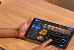 Pessoa usando um tablet para fazer pedidos de hambúrgueres gourmet em um aplicativo de delivery.