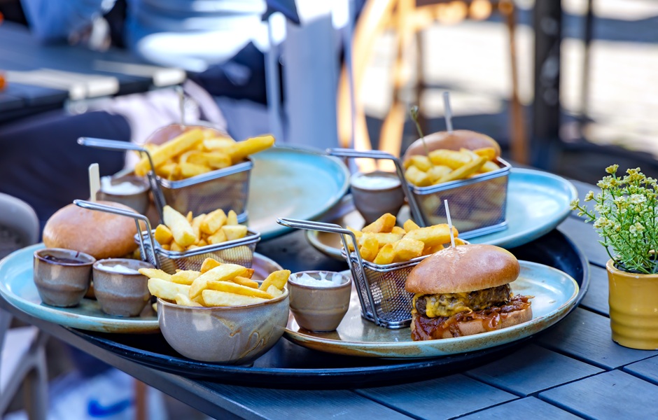 Imagem de uma refeição com batatas fritas e hambúrguer, incluindo molhos e acompanhamentos, servida em um ambiente ao ar livre.