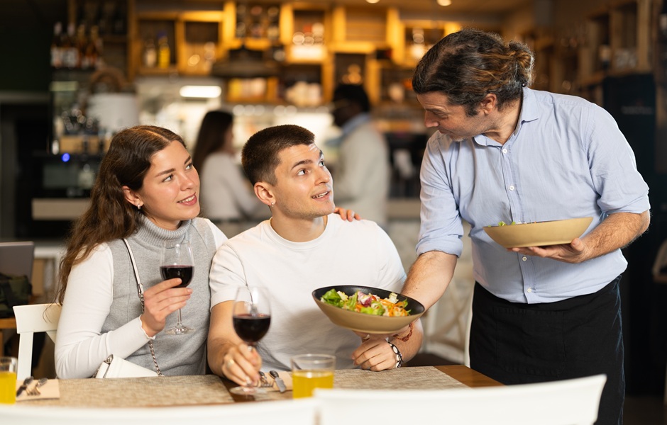 Família apreciando jantar em restaurante, com o garçom atendendo e servi com pratos e taças de vinho, ambiente acolhedor e descontraído.
