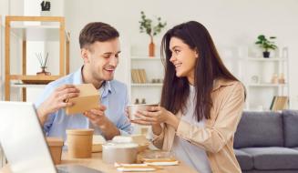 Homem feliz recebendo presente de uma mulher, momento de confraternização e amizade em ambiente de sala de estar moderna com decoração minimalista.