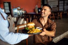 Homem sorridente recebendo um prato de hambúrguer e batatas fritas em um restaurante aconchegante, celebração de momento feliz e refeição deliciosa.