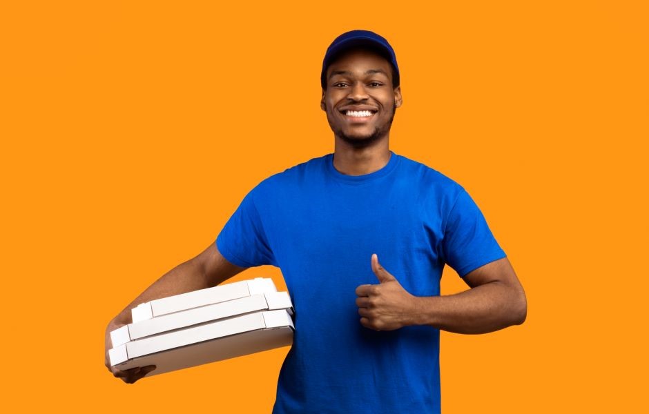 Entregador de pizza sorridente com uniforme azul, segurando caixas de pizza, em fundo laranja, promovendo serviço de delivery de pizza.