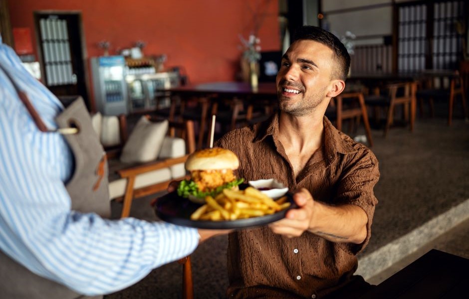 Homem sorridente recebendo um prato de hambúrguer e batatas fritas em um restaurante aconchegante, celebração de momento feliz e refeição deliciosa.