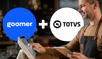 Imagem de um barista sorridente atendendo clientes, com os logotipos do Goomer e TOTVS ao fundo, destacando a parceria entre as marcas