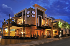 Fachada do restaurante Água Doce Sabores do Brasil à noite, com iluminação externa, mesas ao ar livre, guarda-sóis, palmeiras e placas de marcas de cerveja na fachada.